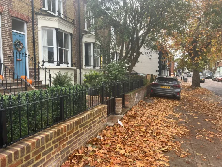Black garden railings on a brick wall on a leaf-strewn street