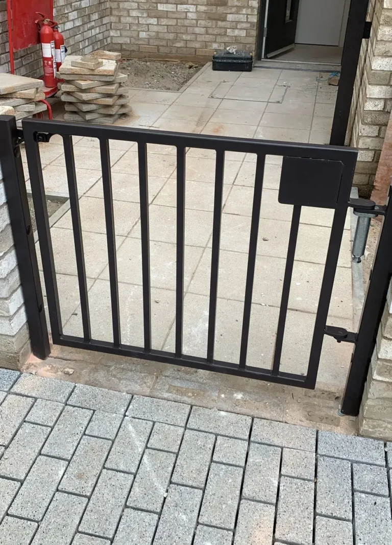 A black pedestrian gate on a paved driveway