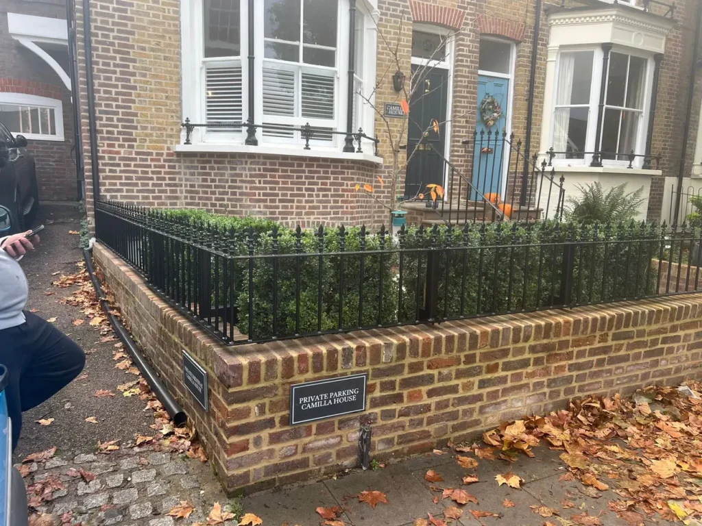 A corner run of black railings on a brick garden wall by a period house