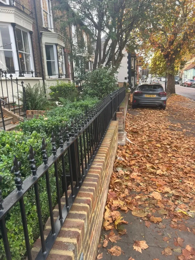 A long run of black garden railings on a brick wall in autumn