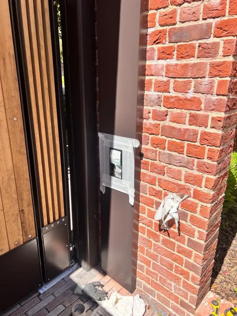 A timber gate with a video intercom in a red-brick entrance