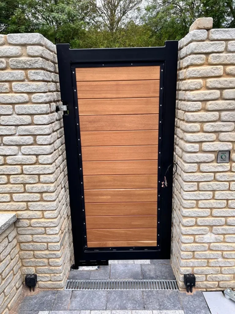 A timber pedestrian gate between stone piers on a paved path