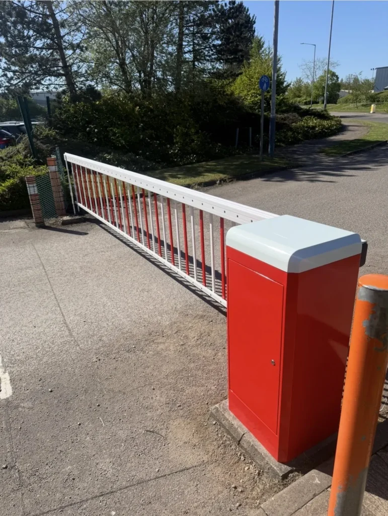 Red automatic barrier cabinet with a long skirted arm across a site road