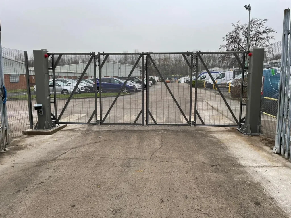 Grey bi-folding speed gates with mesh infill across an industrial site entrance